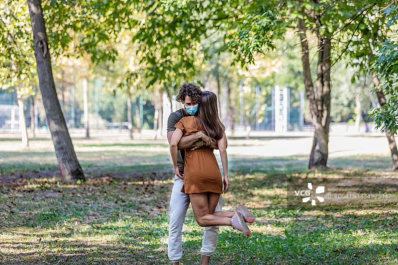 这是一对快乐的相爱的年轻夫妇的肖像，他们在公园散步，在病毒时间互相拥抱。图片素材
