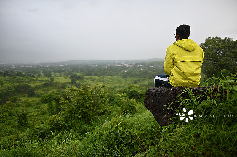一个年轻人坐在山谷边缘的岩石上图片素材