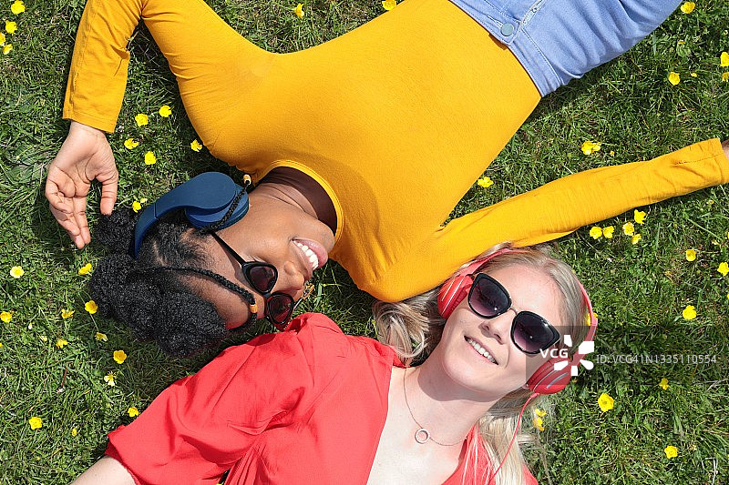 两个年轻女人躺在草地上听音乐图片素材