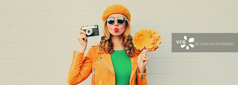 秋天美丽的年轻女人的肖像与黄色的枫叶和胶卷相机戴法国贝雷帽在灰色的背景图片素材
