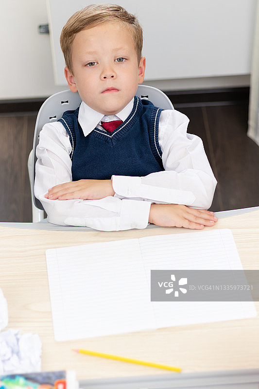 大流行期间，身穿校服、打着领带的一年级男生坐在书桌前做作业。有选择性的重点。特写镜头图片素材
