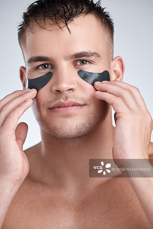 一个年轻英俊的男人的特写，戴着黑眼圈，衬着灰色的背景图片素材
