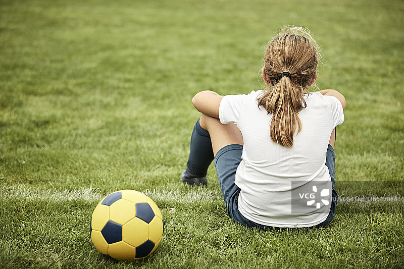 后视图的女孩球坐在足球场图片素材