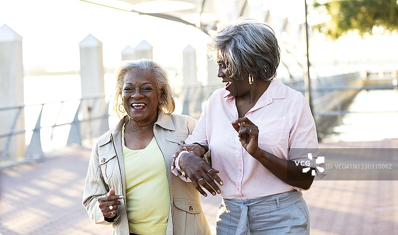 年长的非裔美国妇女挽着臂走着，笑着图片素材