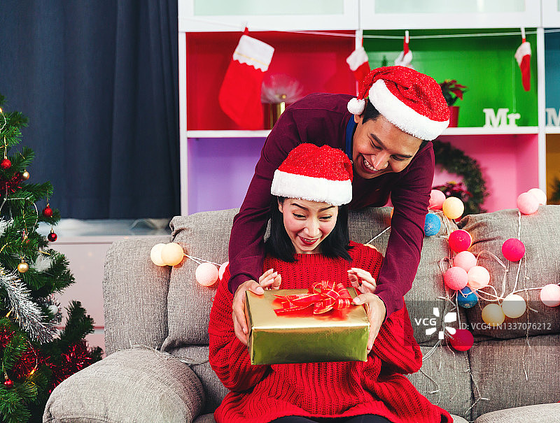 圣诞快乐，年轻的情侣惊喜的圣诞礼物，浪漫的情侣交换礼盒，戴红帽子的情侣圣诞老人，圣诞节节日庆祝。图片素材