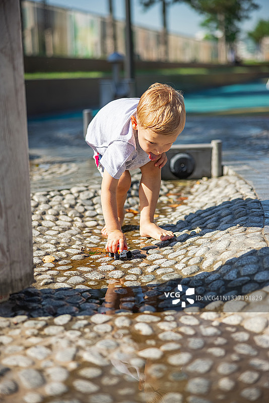 一个头发湿了的金发小男孩，光着脚在水里玩他的玩具车图片素材