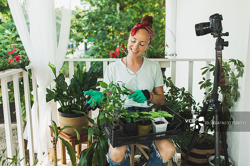 快乐的女人在绿色橡胶手套与盆栽记录园艺教育视频教程在现代lhome露台。图片素材