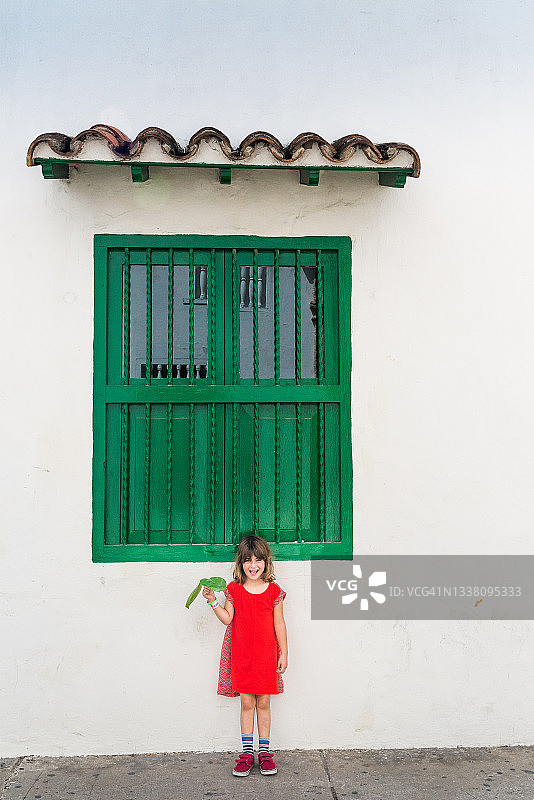 可爱快乐的小女孩穿着红裙子站在充满活力的西班牙建筑前图片素材