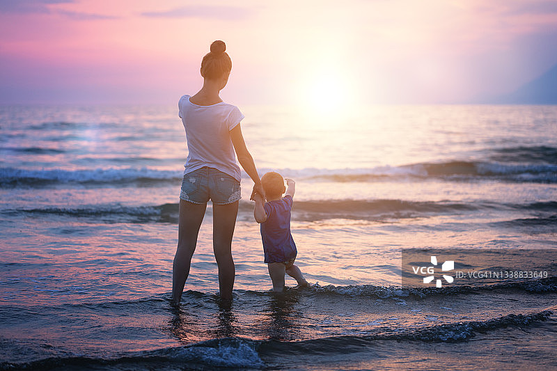 带着婴儿的女人站在海浪中迎接日落图片素材