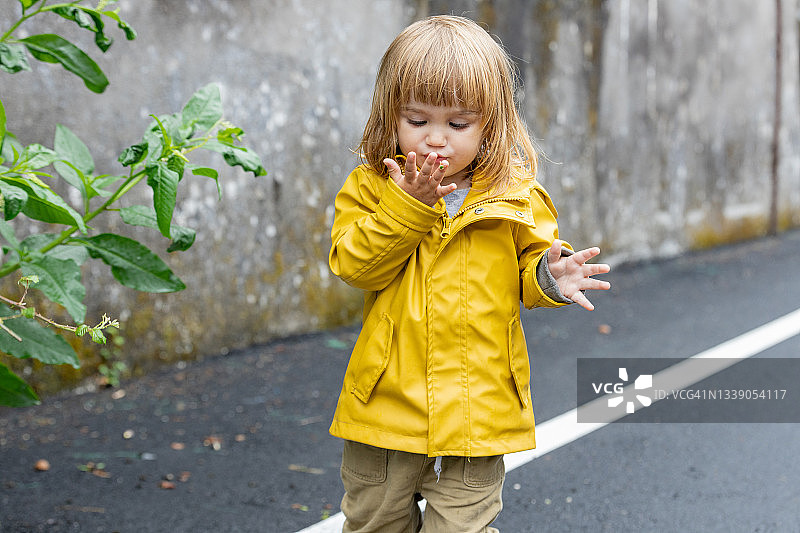 小女孩在雨天走在户外的街道上。图片素材