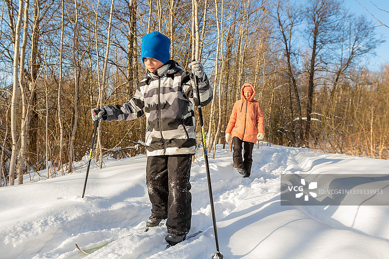 母亲和孩子在森林的冬天滑雪，在厚厚的积雪中漫步图片素材