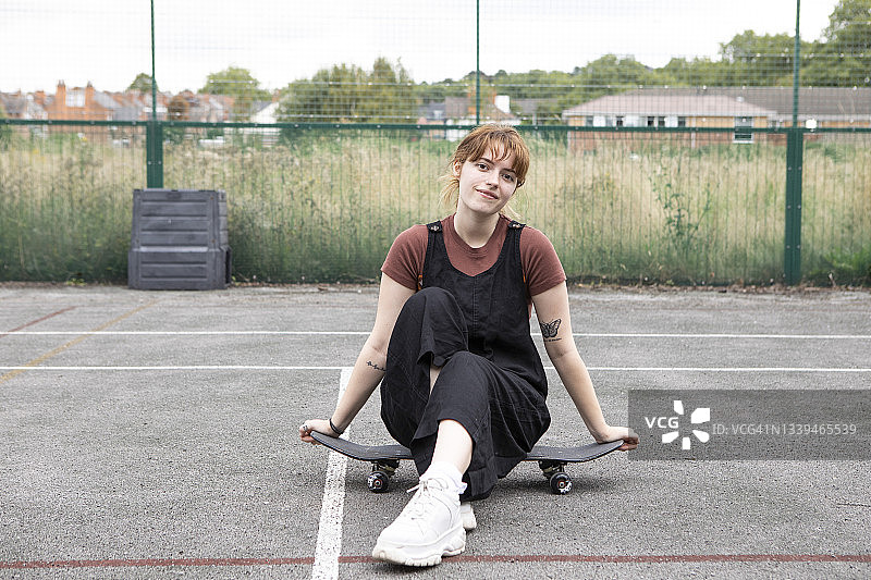 女学生坐在一个废弃的网球场的滑板上图片素材
