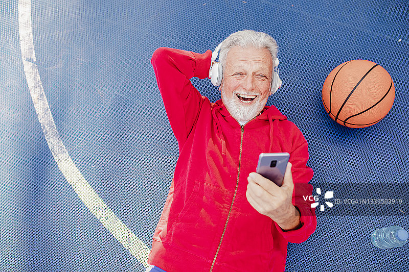 一位老人的高角度肖像正在篮球场上休息，听着音乐图片素材