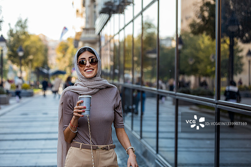 早晨在城市街道上，中年妇女端着一杯咖啡。图片素材