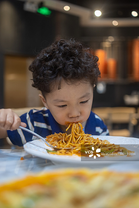 一个小男孩在餐馆里吃意大利面图片素材