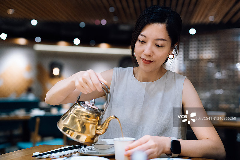 年轻的亚洲妇女拿着茶壶和倒茶在一个中国餐馆吃饭。中国的传统文化。外出就餐的生活方式图片素材