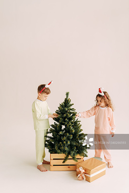 快乐有趣的小孩子、青少年、朋友们戴着圣诞老人的帽子，用礼物和气球装饰一棵小圣诞树，在白色的背景上庆祝圣诞节图片素材