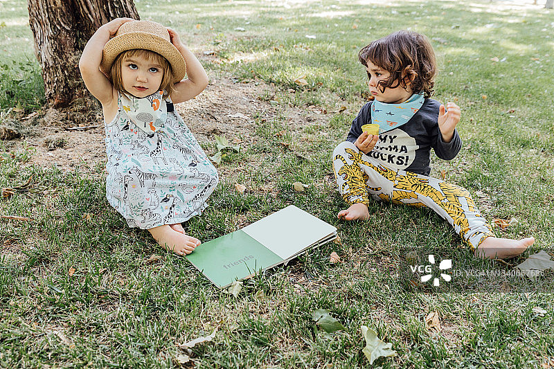 可爱的小弟弟和小妹妹坐在公园的草地上，一起看书图片素材