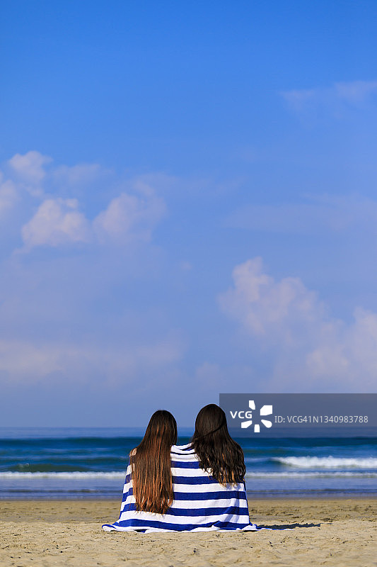 在阳光明媚的日子里，裹着毛巾的妇女们坐在海滩上图片素材