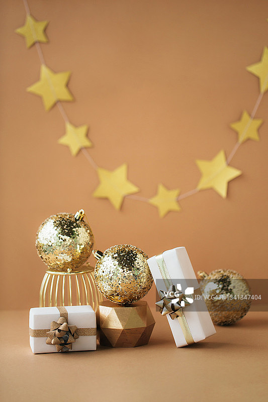 两个白色的礼物和三个金色的球组成的圣诞作文，金黄色的讲台上米色的背景。新年概念图片素材