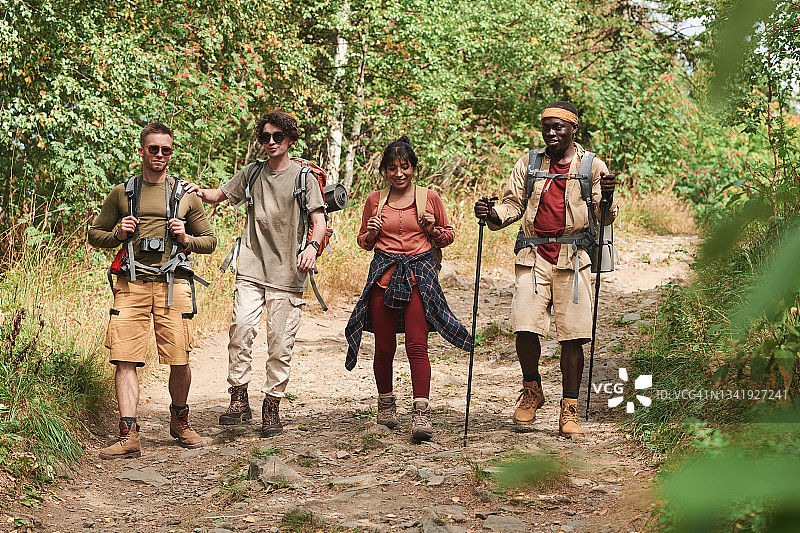 一群年轻的多民族朋友，穿着休闲装，背着背包，一起在森林里徒步旅行图片素材