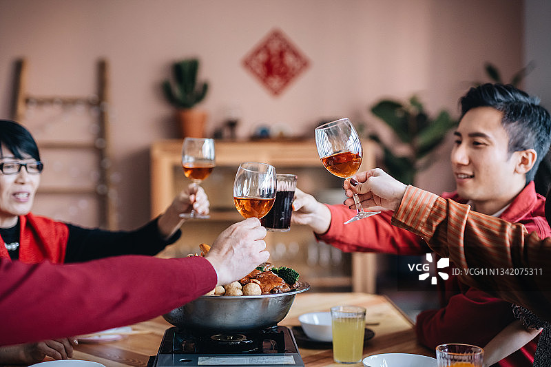 这是一个欢乐的亚洲家庭三代欢度中国新年，在享用美味的中国传统盆菜团圆饭的同时祝酒的镜头图片素材