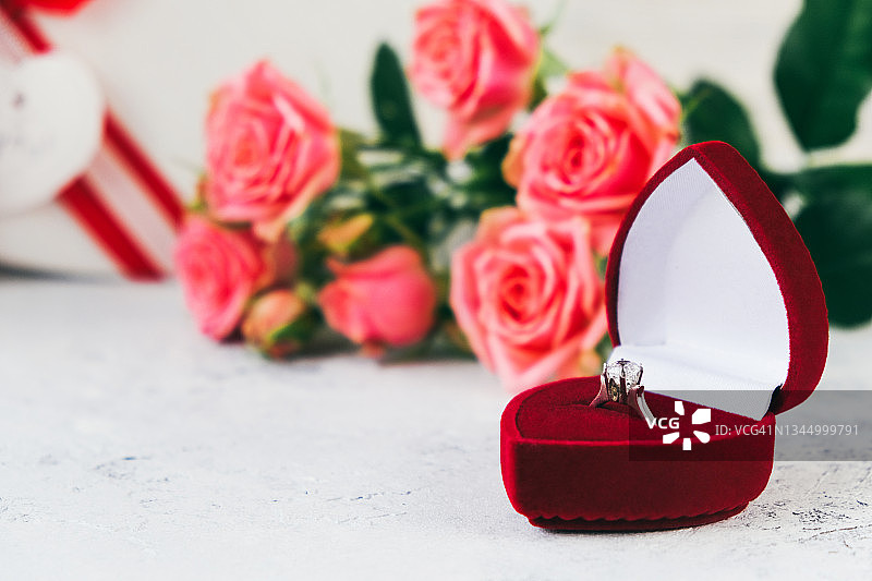心形盒子里装着粉红色的玫瑰花和银戒指，上面镶着一块透明的石头图片素材