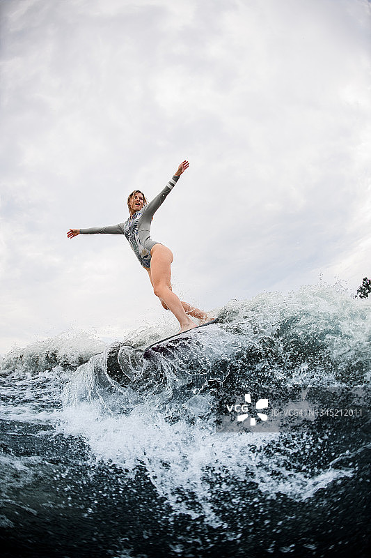 穿着灰色潜水衣的能量女人骑着波浪冲下巨大的溅起水花的河波图片素材