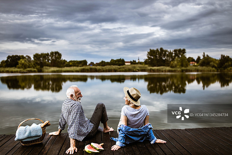 快乐的老夫妇在河边的码头上野餐。图片素材