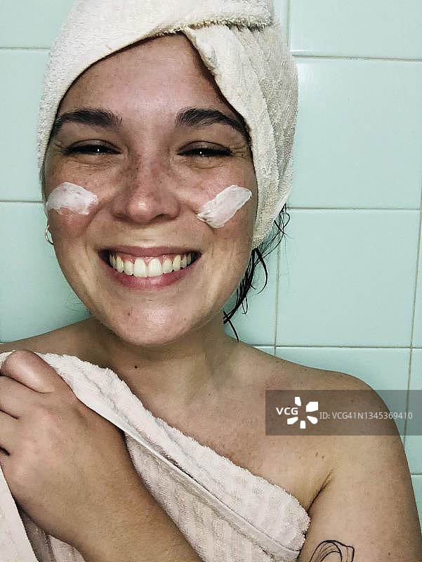一个沐浴后脸上涂着奶油微笑的女人的肖像图片素材