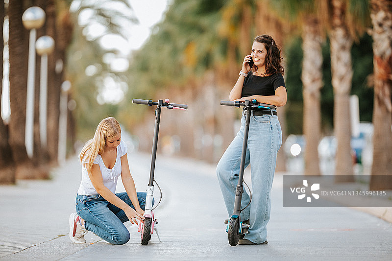 两名年轻女性在城市中使用电动滑板车，因为缺陷而呼叫技术支持图片素材