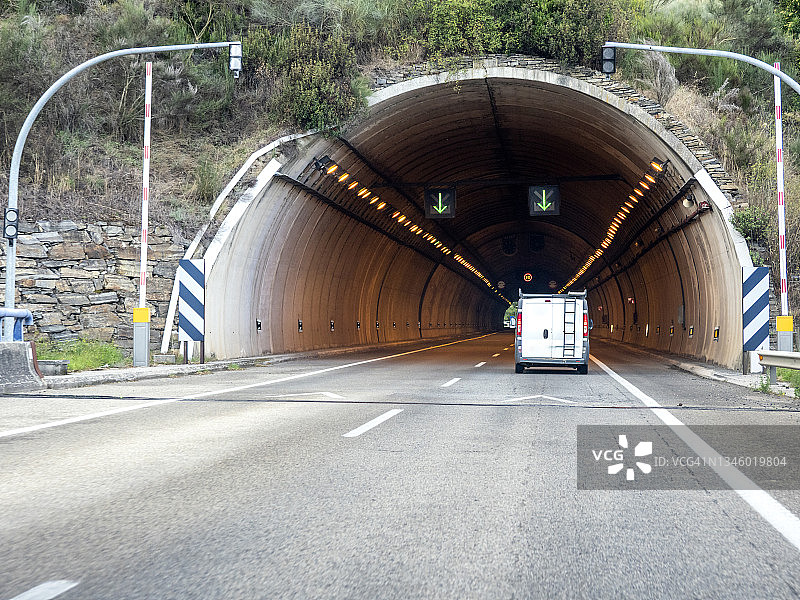 车的观点，双车道公路上，一辆车正在接近一个有灯光的隧道。图片素材
