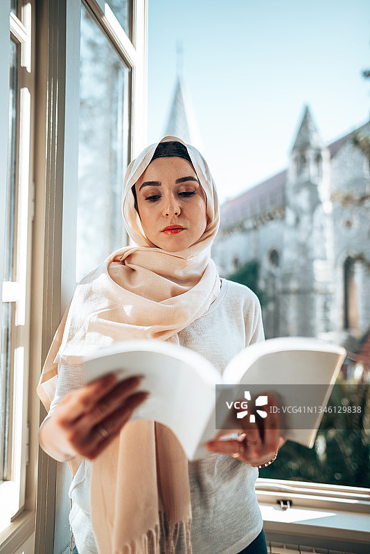 一位穆斯林妇女在窗前看书图片素材