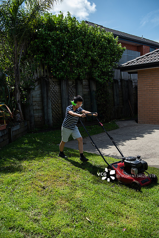 十几岁的男孩戴着耳机在后院修剪草坪图片素材