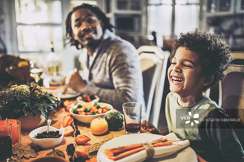 快乐的黑人男孩和他的父亲在餐桌上吃饭。图片素材
