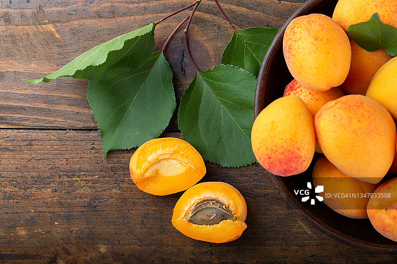 木桌上的碗里盛着熟透的杏子和杏叶。图片素材