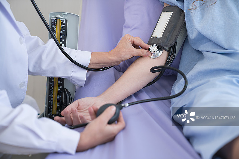 医生给躺在医院病床上的女病人量血压。图片素材