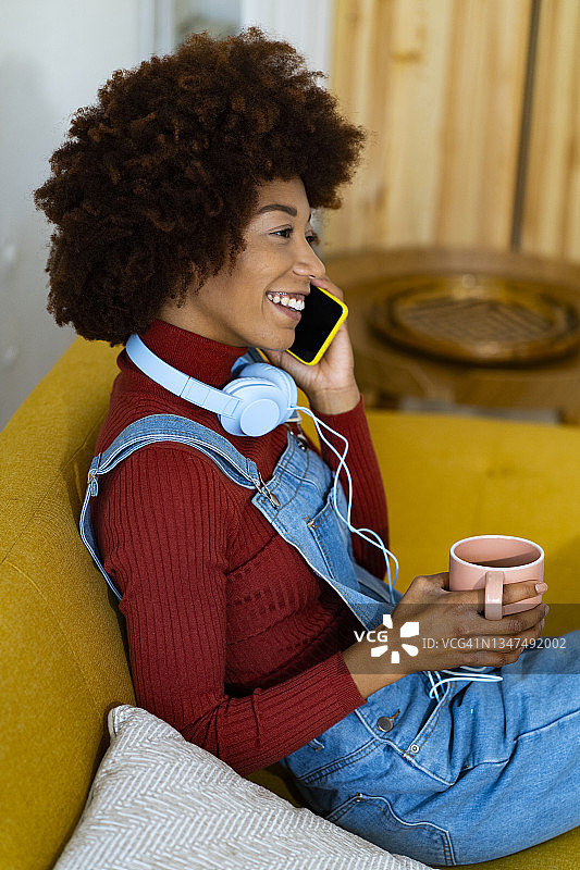 年轻的非洲女人拿着咖啡杯在家里用手机聊天图片素材
