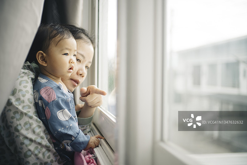 美丽的早晨充满积极的情绪亚洲母亲和女儿醒来，望着窗外图片素材