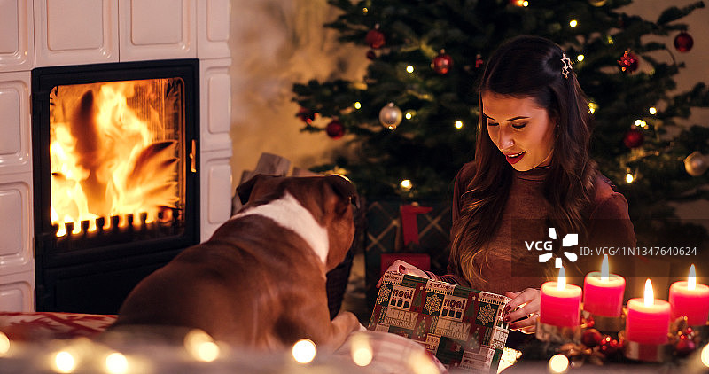 年轻的女人在壁炉旁拆开圣诞礼物，圣诞节花环上装饰着圣诞树，丈夫穿着舒适的袜子图片素材