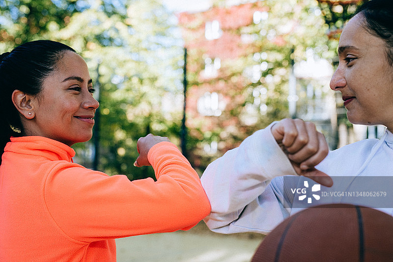 一个快乐的女人和她的女朋友在篮球场用胳膊肘打招呼。图片素材