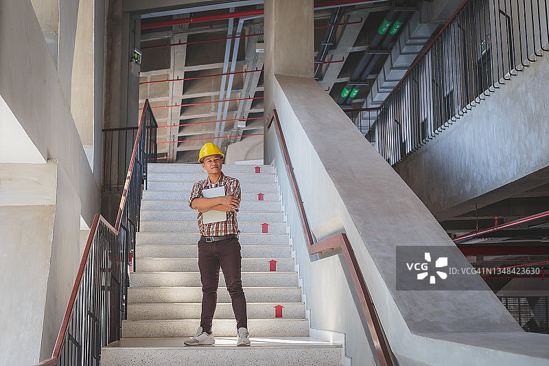 图为一名亚洲工程师戴着安全帽，手持数码平板电脑，站在工地楼梯上图片素材
