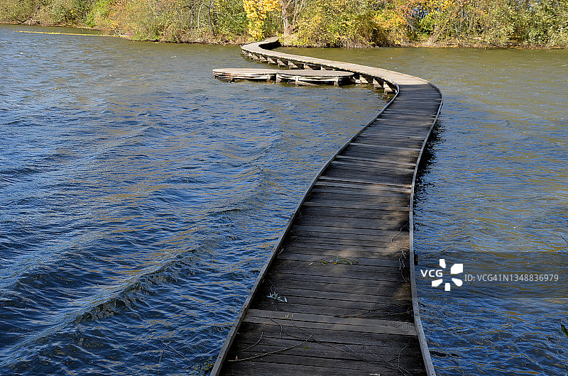 由木板制成的浮动走道。踩高跷上的狭窄弯曲的小路被推入湖底，高出湖水。没有栏杆。更多的设计走道由单独的圆形板制成。秋天防波堤图片素材