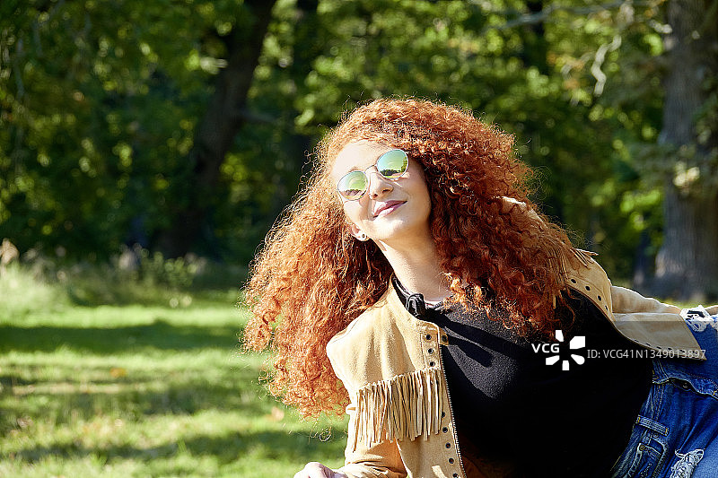 红发年轻美丽的女人戴着太阳镜享受夏日的阳光图片素材