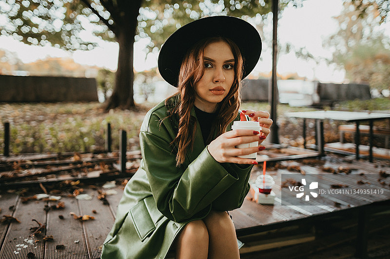 戴着帽子在公园里喝咖啡的时尚女人图片素材