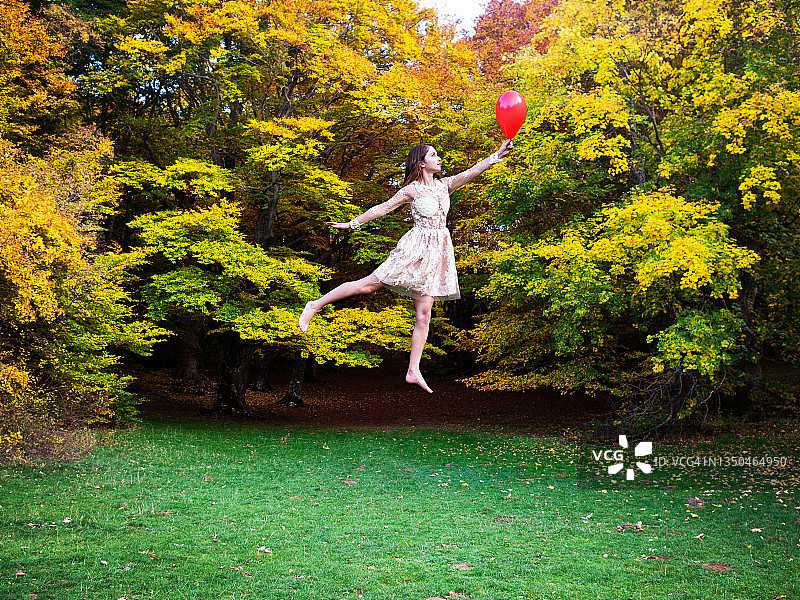 快乐的年轻黑发女子与红色气球飞行在秋天的风景图片素材