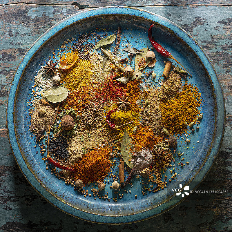 在一个古老的绿松石色陶瓷盘子上，各种色彩丰富、有机、干燥、充满活力的印度食品香料。图片素材
