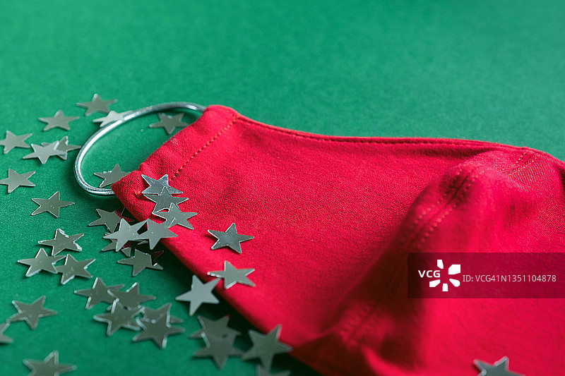 红色医用防护口罩和五颜六色的五彩纸屑在绿色圣诞背景。预防和预防COVID - 19大流行的传播。预防病毒、感染和肺炎。一个快乐健康的圣诞节的概念。图片素材