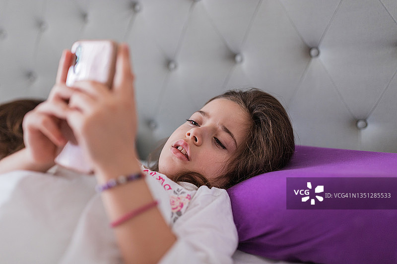 悲伤的年轻女孩在她的床上醒来后使用智能手机图片素材