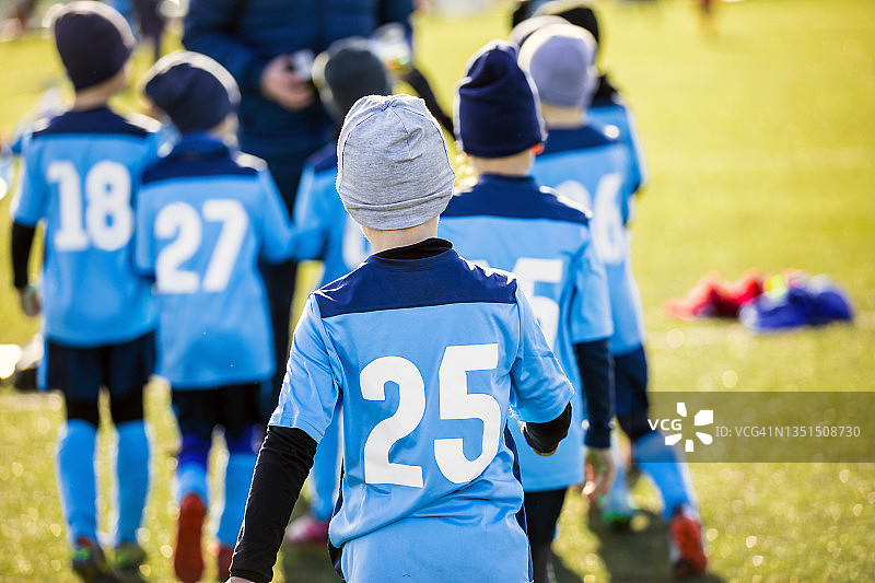 男孩在蓝色足球球衣跟随教练在一个队。学校儿童锦标赛。孩子们在冬日阳光明媚的户外运动。穿着足球冬装的孩子们图片素材